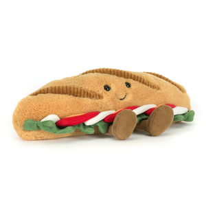 Jellycat plush toy shaped like a caprese baguette with a smiling face and brown feet on a white background.