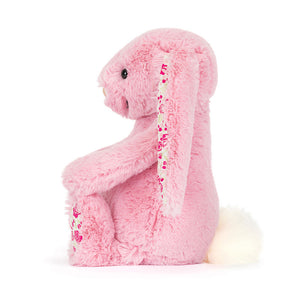 Side view of a Jellycat pink plush bunny with floral patterned ear lining and a white fluffy tail on a white background. 