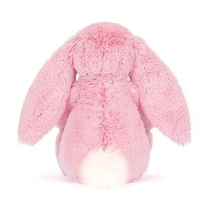 Back view of a Jellycat pink plush bunny with a white fluffy tail on a white background. 