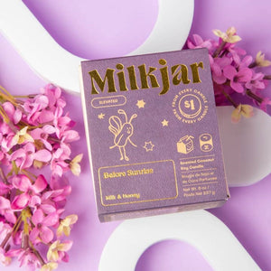 Purple packaging box with gold Milkjar branding on a purple and white surface with flowers in the background. 