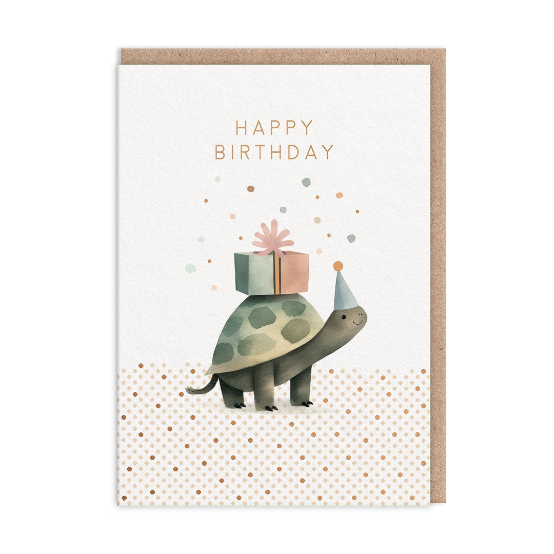 Greeting card with a tortoise wearing a part hat and holding a gift box on a white and polka dot background. The card has "Happy Birthday" text. 