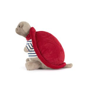 Side view of a beige Jellycat turtle plush with a frowning face wearing a blue and white striped shirt and a red shell on a white background