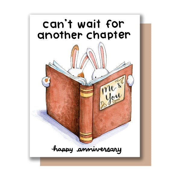 Greeting card with illustration of two white rabbits reading a book titled 'Me & You' and the text 'can't wait for another chapter, happy anniversary' on a white background.