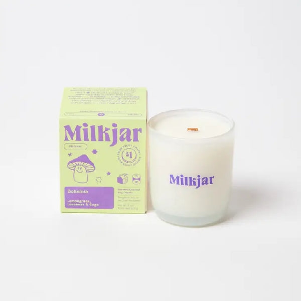 Canadian company Milkjar candle and its box packaging. The white candle is in a translucid glass with "Milkjar" written in purple. The other side of the candle has a cute smiling mushroom doodle in purple. The packaging is a small lime-coloured box with purple text and graphics. 