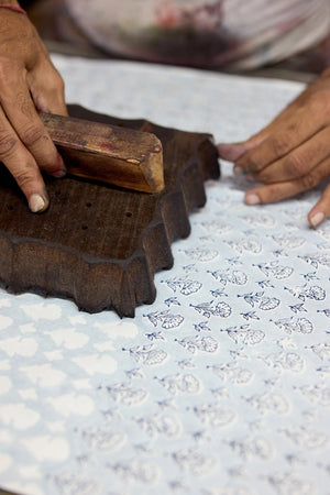Person using a wooden block to print a botanical pattern on cotton paper.