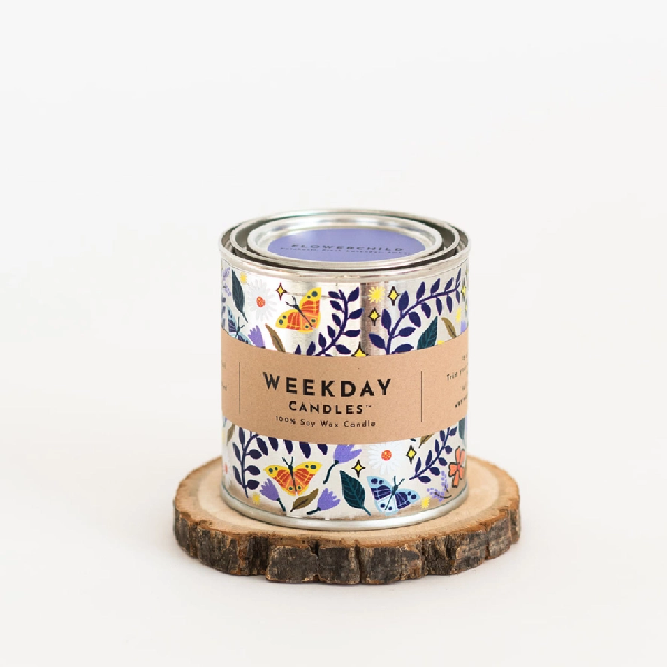 silver tin candle with painted doodles of orange butterflies and purple vines. a brown tag wraps the tin. on it, "Weekday Candles 100% Soy Wax Candle", the name of the product, the ingredients and instructions are written in a sharp black font.