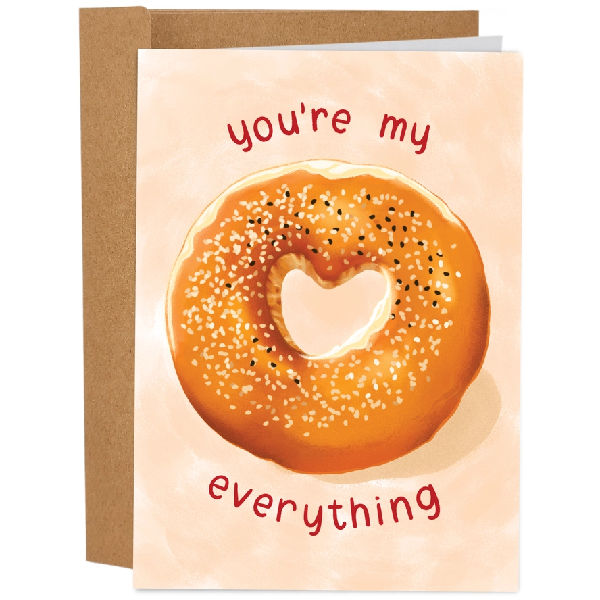 Greeting card featuring an illustration of an everything bagel with a heart-shaped hole in the middle on a cream coloured background. The text 'You're my everything' is printed around the bagel. 