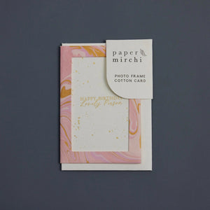 Photo frame cotton card with a pink and gold marbled design and 'Happy Birthday Lovely Person' text. The card sits on a blue background. 