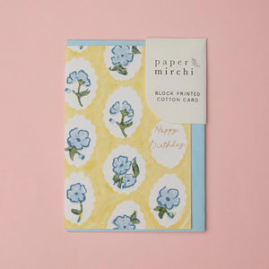Cotton paper greeting card with a yellow, blue and green botanical design on a yellow background. The card is shown with a blue envelope on a pink background. 