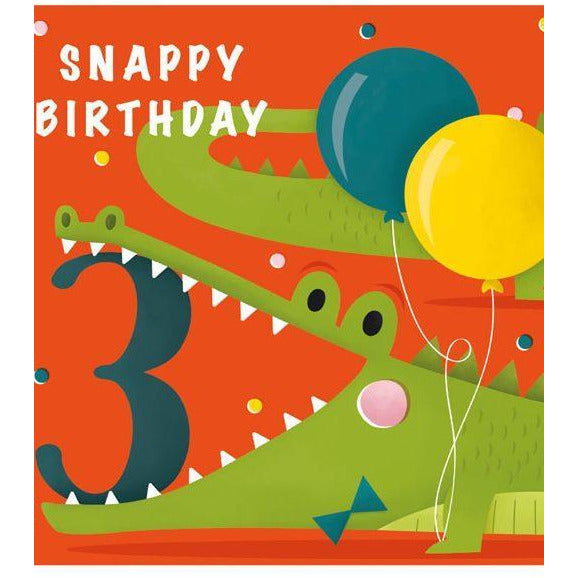 a bright and colourful orange card with a cartoonish illustration of a bow-tie-wearing crocodile. the number three is between its teeth. "snappy birthay" is written in white on the top left corner of the card